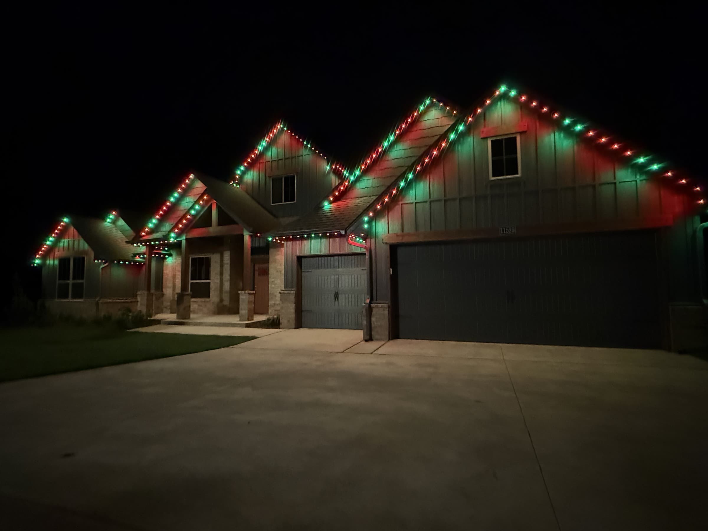 Multi-gable mixed-material home with TruLight permanent lighting set to a red-and-green holiday roofline effect.