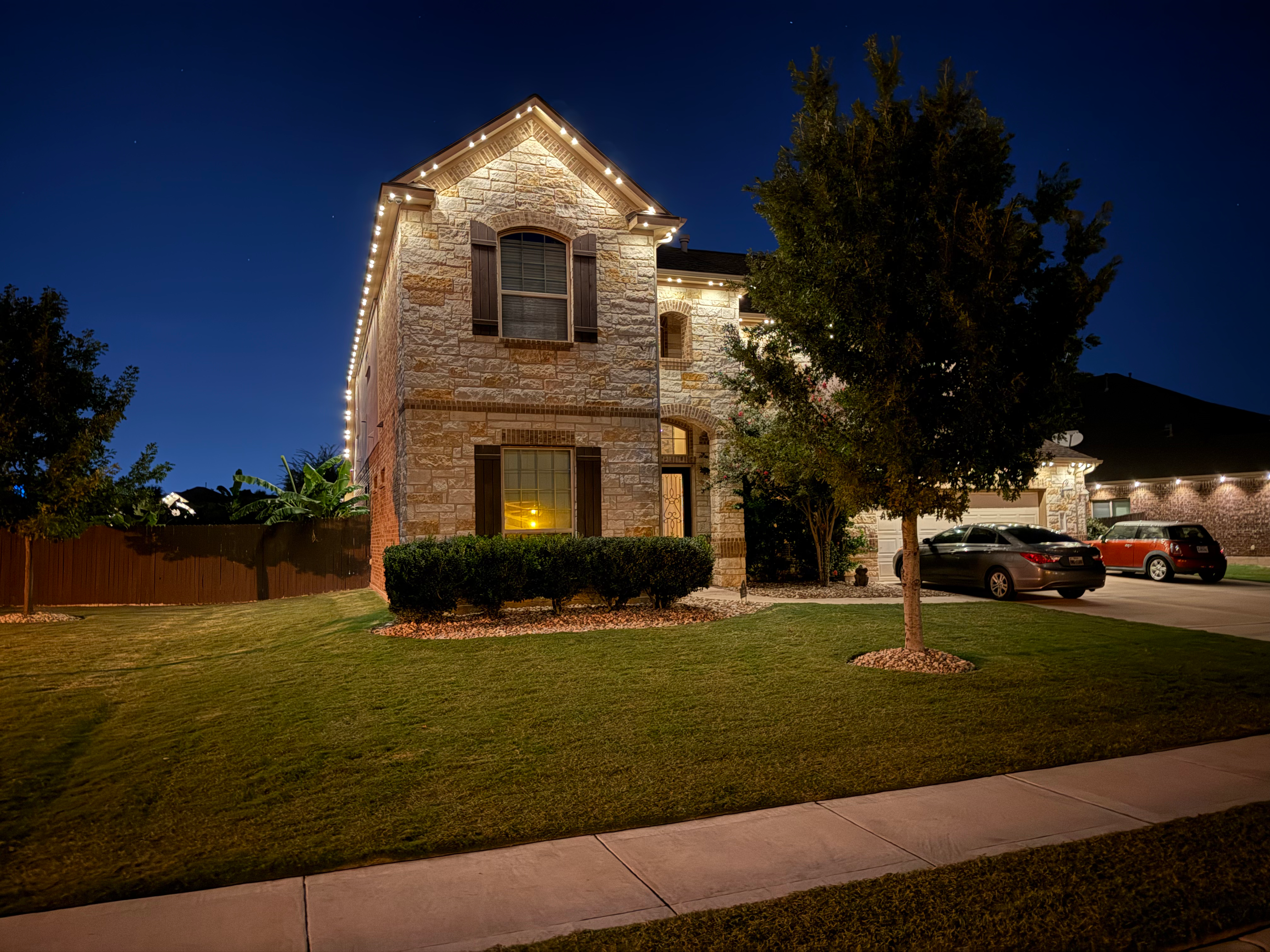 Two story stone home with warm white LED roofline lighting